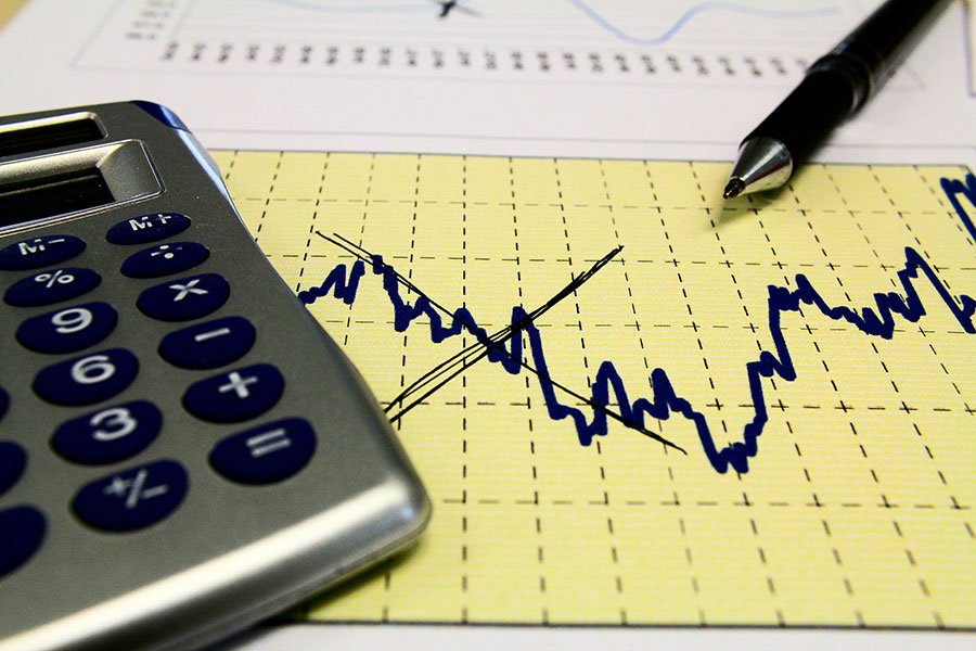 Imagem colorida de calculadora e uma caneta sobre uma folha que exibe um gráfico com indicadores econômicos - Metrópoles