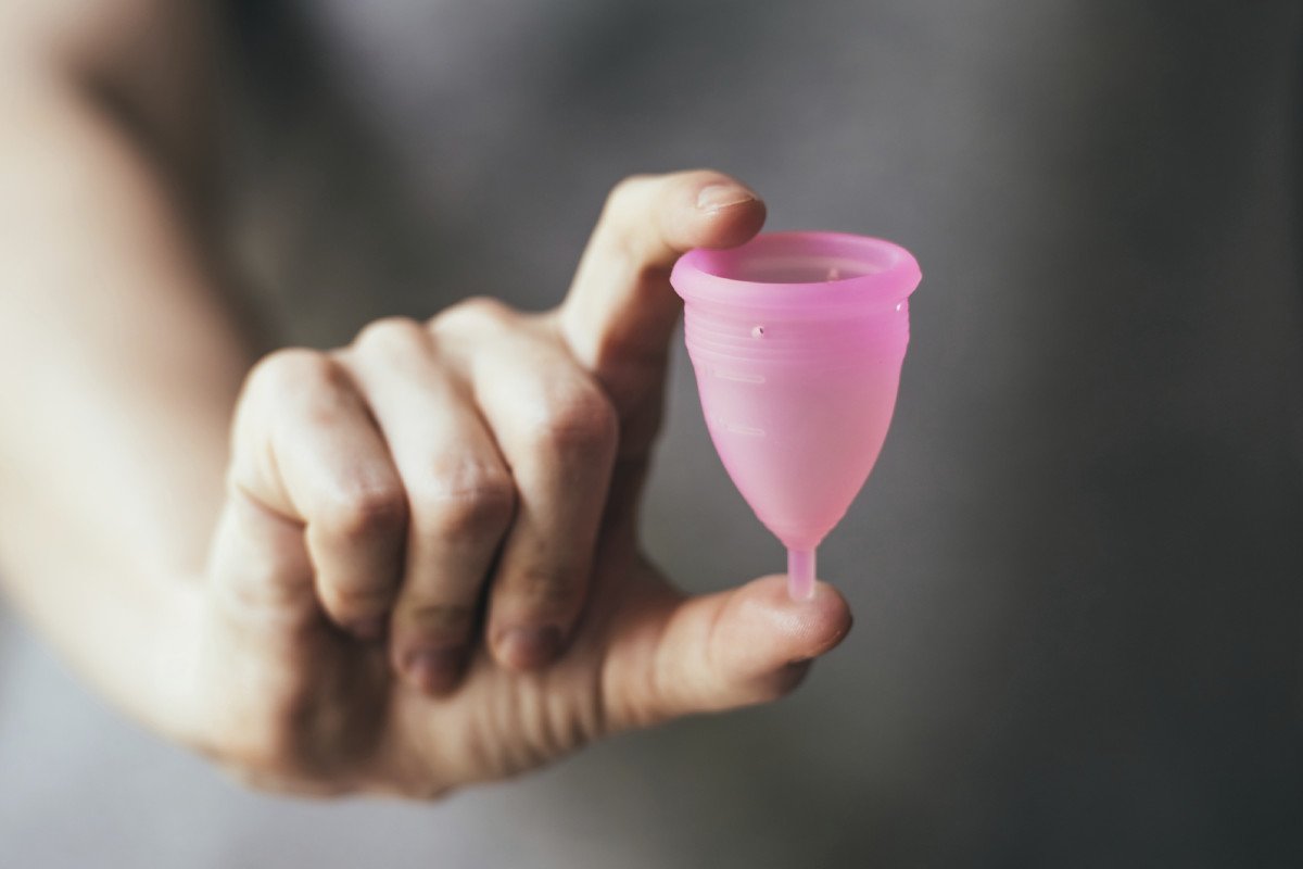 Mão segurando coletor menstrual rosa