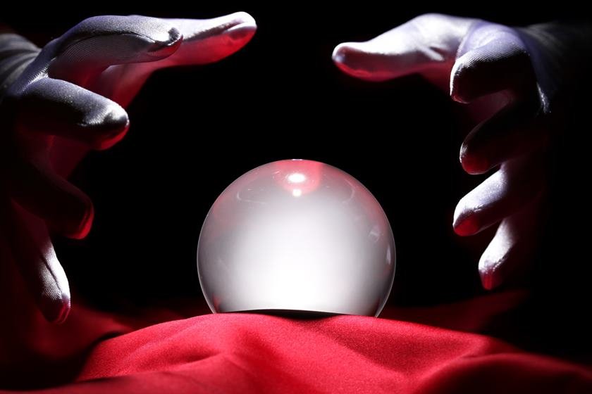 Hands surrounding a glowing crystal ball on red fabric