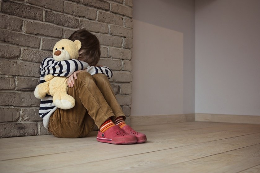 Sad little boy sitting against the wall in despair
