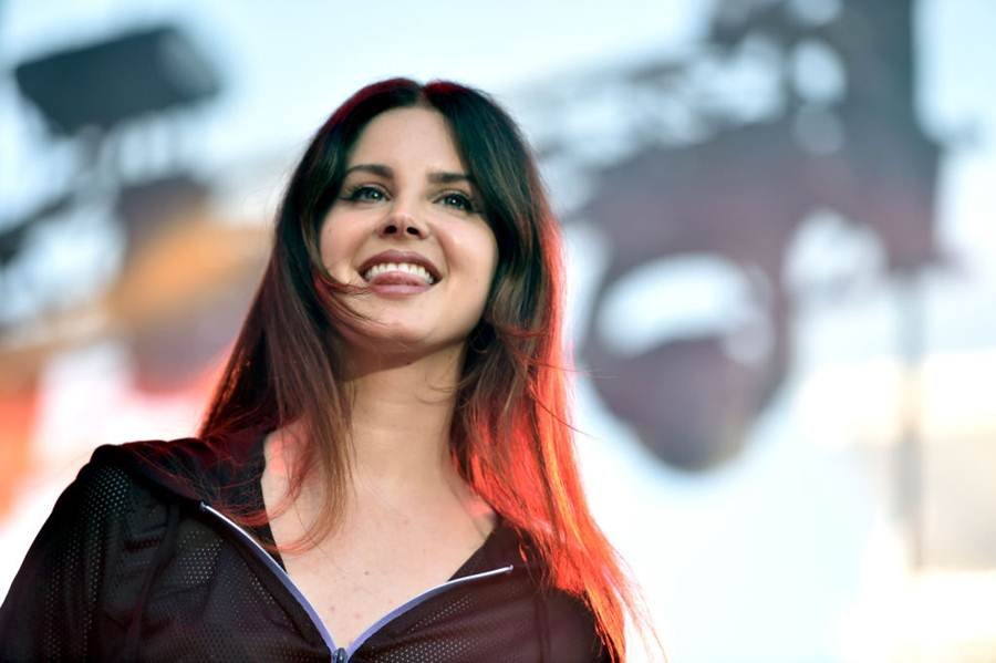 Foto colorida de Lana Del Rey sorrindo e usando roupa preta - Metrópoles