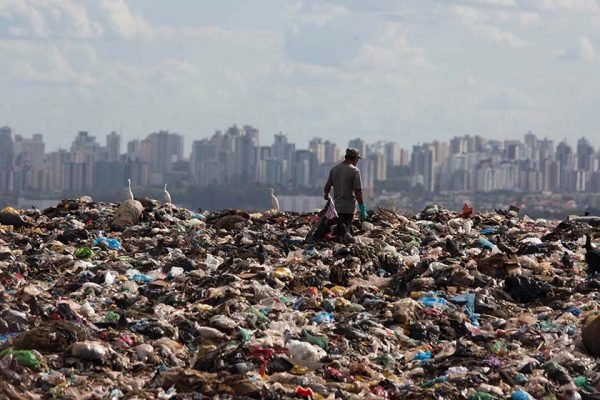 Homem em cima de pilha de lixo e prédios ao fundo