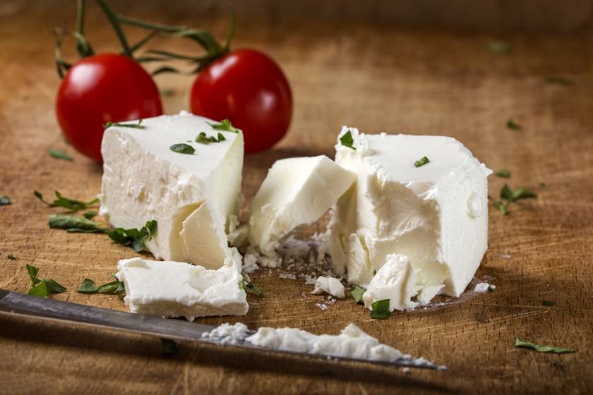 Feta cheese with knife and two cherry tomatoes in background on wood