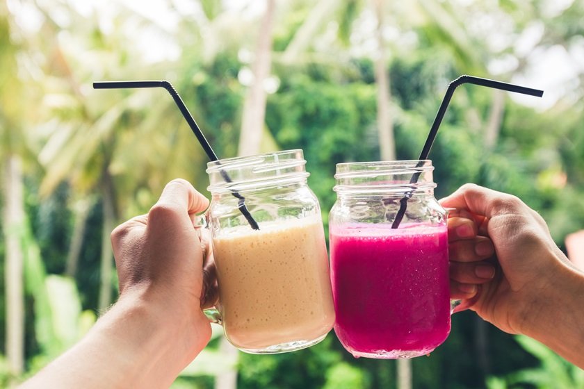 Two colorful fruit shakes in hands. Summer and tropical mood. Cold blended drinks, banana and dragon fruit smoothie. Clink glasses by couple hands