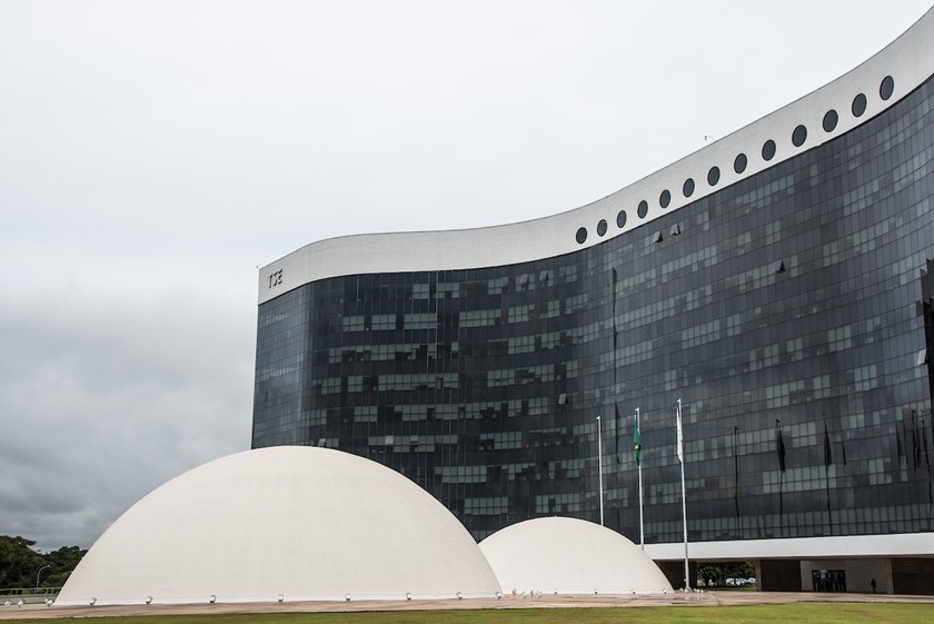 Prédio do Tribunal Superior Eleitoral em Brasília. Vê-se as duas cúpulas brancas em frente ao enorme edifício ondulado de janelas escuras - Metrópoles