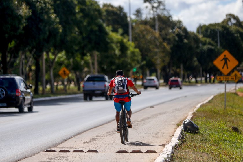 Pessoa andando de bicicleta em ciclovia ao lado de pista de carros