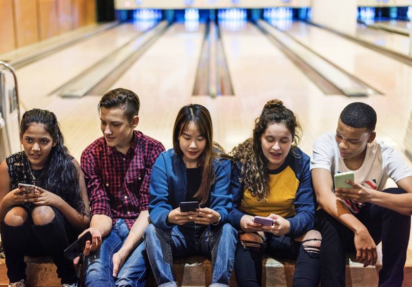 Group of teenage friends using smartphone in a bowling alley