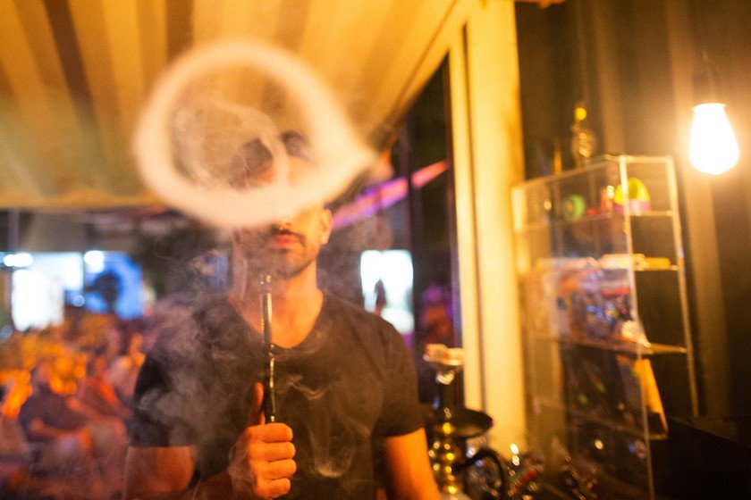 Imagem colorida de pessoa fumando narguilé e soltando círculos de fumaça - Metrópoles