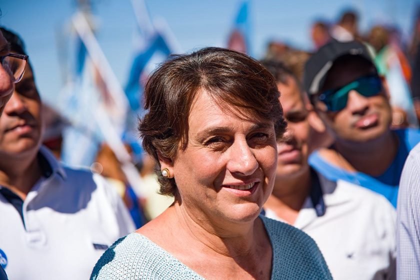 Mulher sorri para foto com bandeiras ao fundo