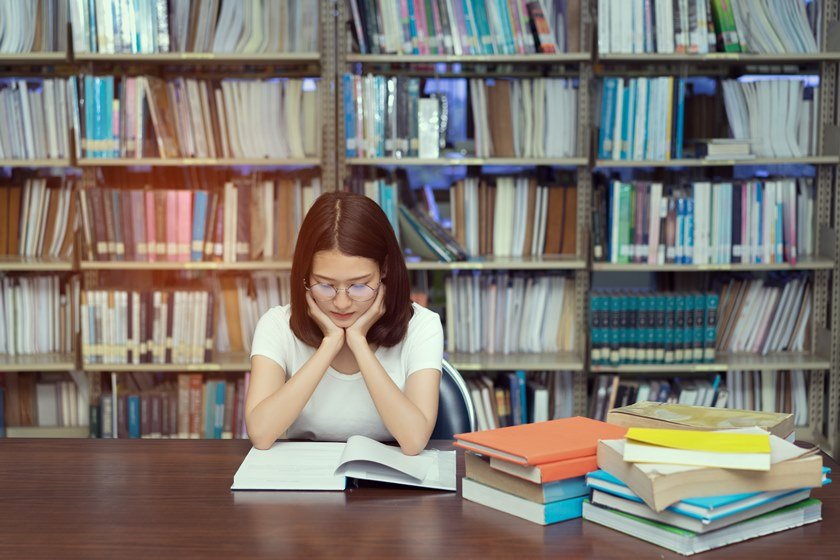 Young student asian girl with glasses reading book serious vision eyesight Hard exam, test and tired stress headache alert worry in classroom library high school university campus college and knowledge center.