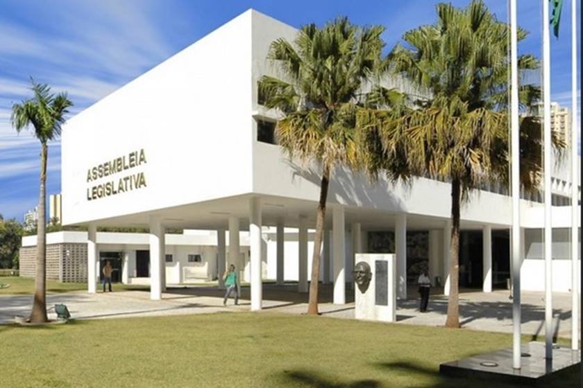 Imagem colorida de prédio com fachada branca e palmeiras