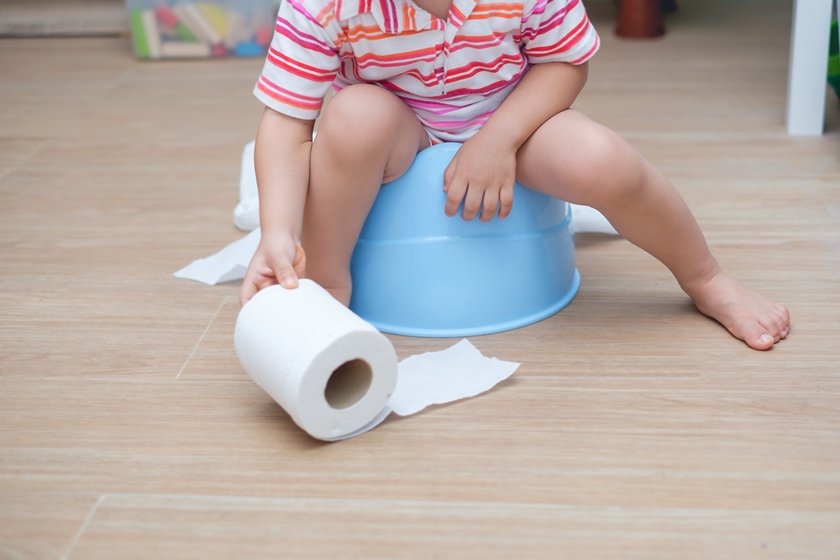 Closeup of legs of little Asian 2 years old toddler baby boy child sitting on blue potty holding, playing with toilet paper