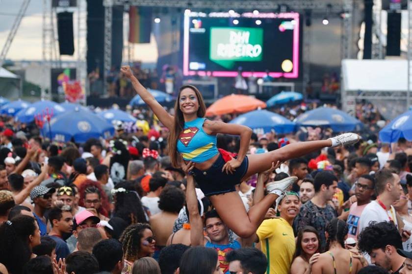 Imagem de mulher vestida de super heroína, sendo levantada por homem em meio a bloco de Carnaval - Metrópoles
