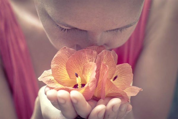Foto mostra mulher cheirando flor laranja - Metrópoles - cheiro olfato