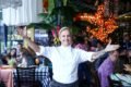 Chef Mara Alcamim e braços abertos em frente a mesas de clientes no Restaurante Universal