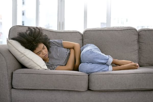 Foto ilustrativa de TPM mostra jovem deitada em sofá em posição fetal