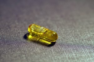 Imagem de uma cápsula amarela de suplemento de vitamina D em superfície cinza - Metrópoles