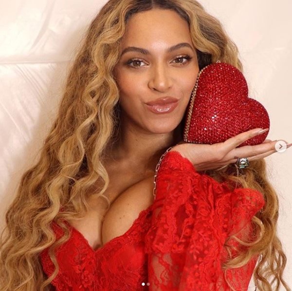 Imagem colorida de uma mulher preta usando uma roupa vermelha e um objeto no formato de coração na mão
