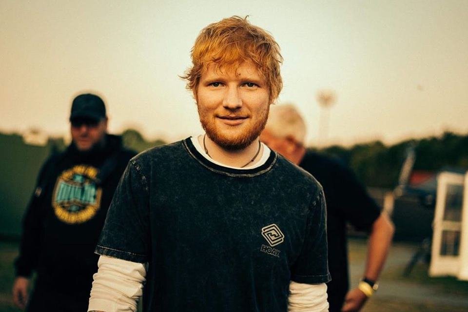 Foto colorida de Ed Sheeran de camisa preta e cabelo ruivo - Metrópoles