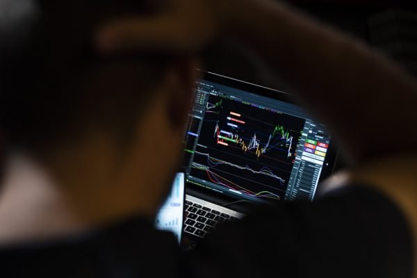 Fotografia colorida de homem em frente à tela de computador olhando para ações na bolsa de valores