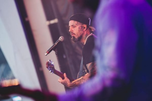 Foto colorida de Tico Santa Cruz cantando no microfone durante show - Metrópoles