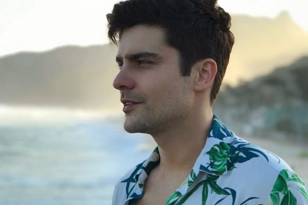 Guilherme Leicam em foto colorida. Ele usa blusa florida e está na praia, de perfil - Metrópoles