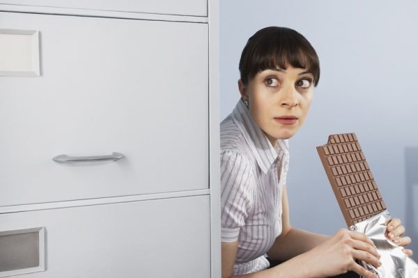 Businesswoman hiding and eating chocolate bar