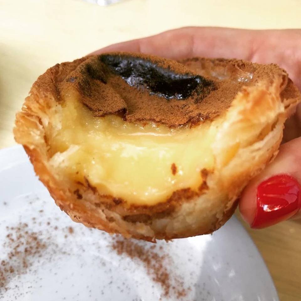 Mão segurando um pastel de belém partido ao meio
