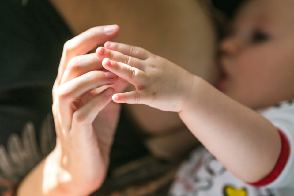 Mão de mulher e bebê na frente e bebê sendo amamentado ao fundo