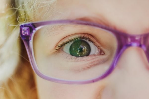 Imagem de perto do olho de uma criança branca com óculos roxo - Metrópoles