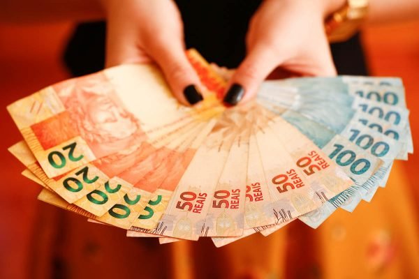 Imagem colorida mostra alguém segurando dinheiro para pagar dívidas Desenrola