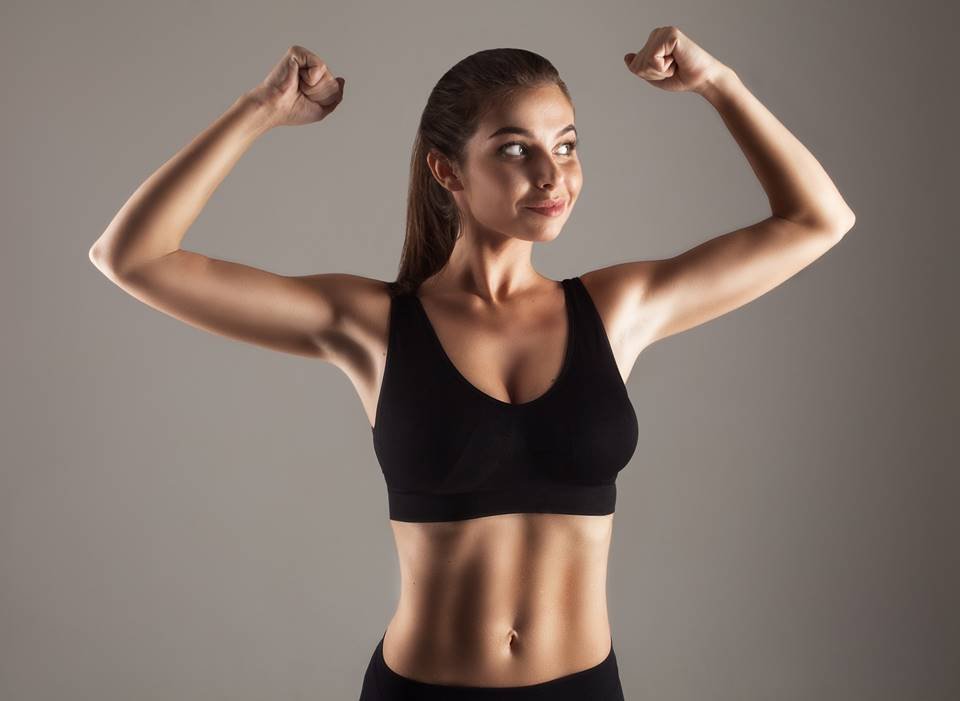 Young Woman Flexing Biceps While Standing Against Gray Background