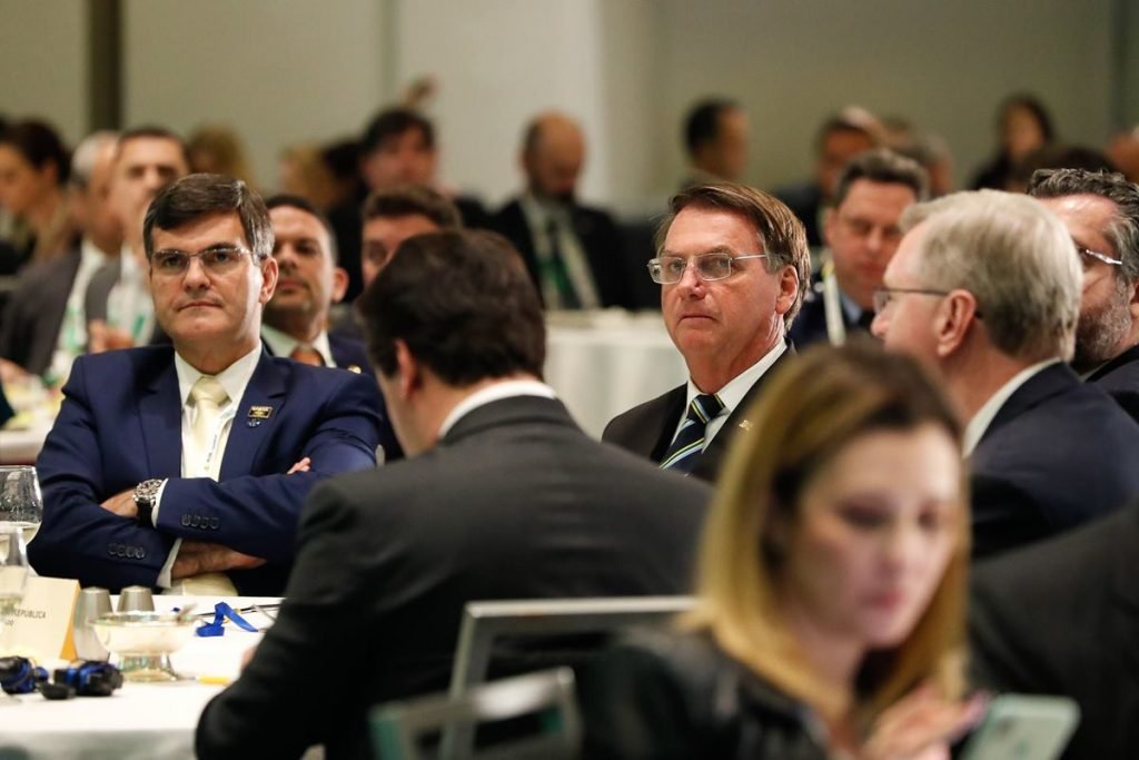 Bolsonaro de óculos sentado em mesa com comitiva nos EUA