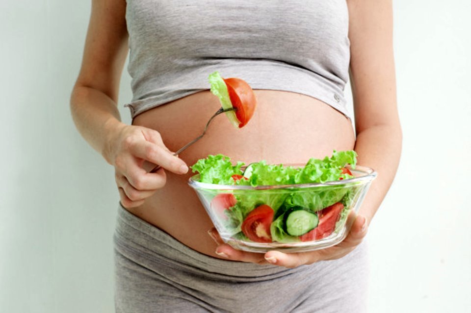 Mulher grávida segurando prato de salada