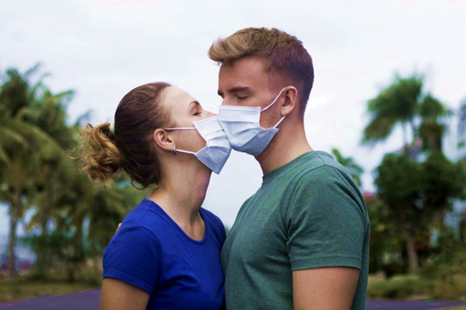 Homem e mulher se beijam usando máscaras de prevenção ao coronavirus