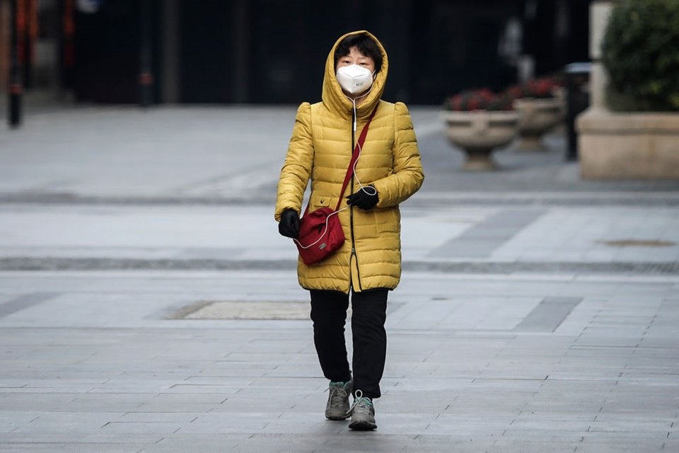 mulher caminha na rua com máscara descartável