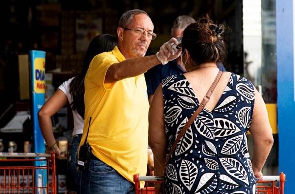 Brigadista mede temperatura de clientes na porta de supermercado Dia a Dia, em Taguatinga