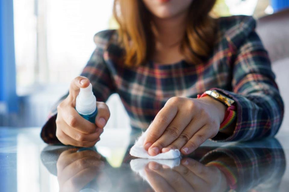 Mulher de blusa xadrez limpando superfície com produto pequeno