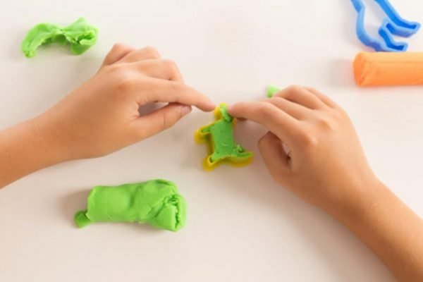 Mãos de uma crianla brincam com massa de modelar verde e formas de dinossauro