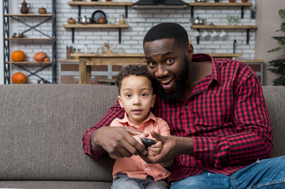Homem negro e filho assistindo tv