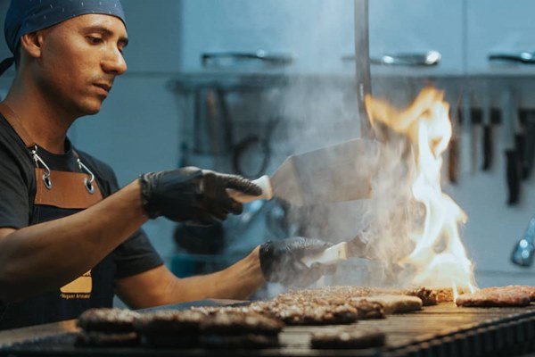 Homem preparando hamburgueres na chapa