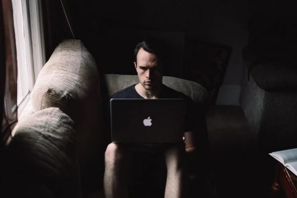 Homem sentado no sofá com macbook no colo, trabalhando