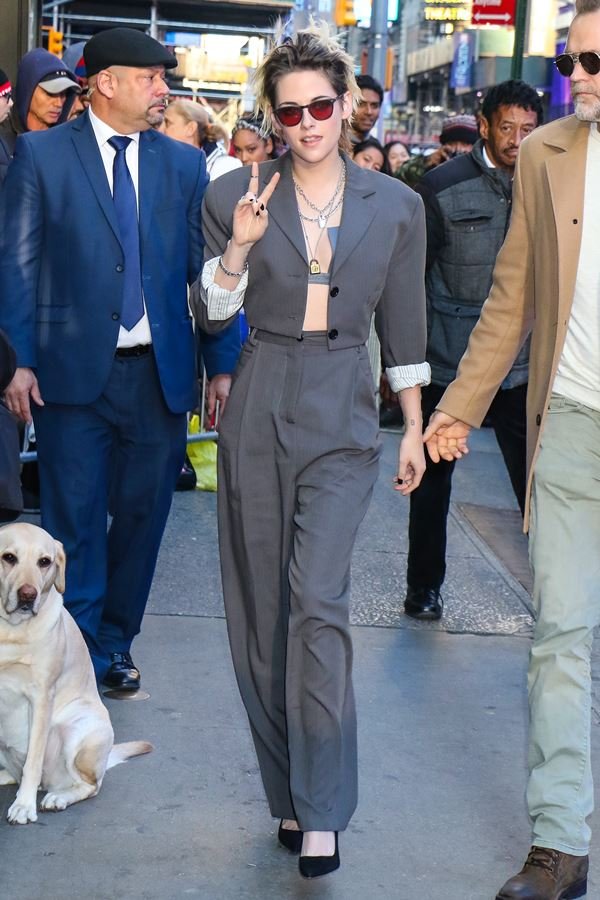Kristen Stewart com conjunto de alfaiataria cinza e sutiã à mostra