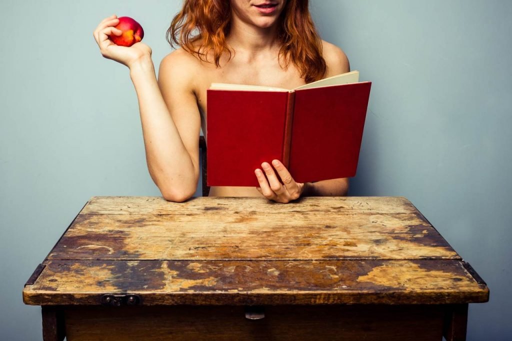 Muher nua lendo livro vermelho e segurando maçã