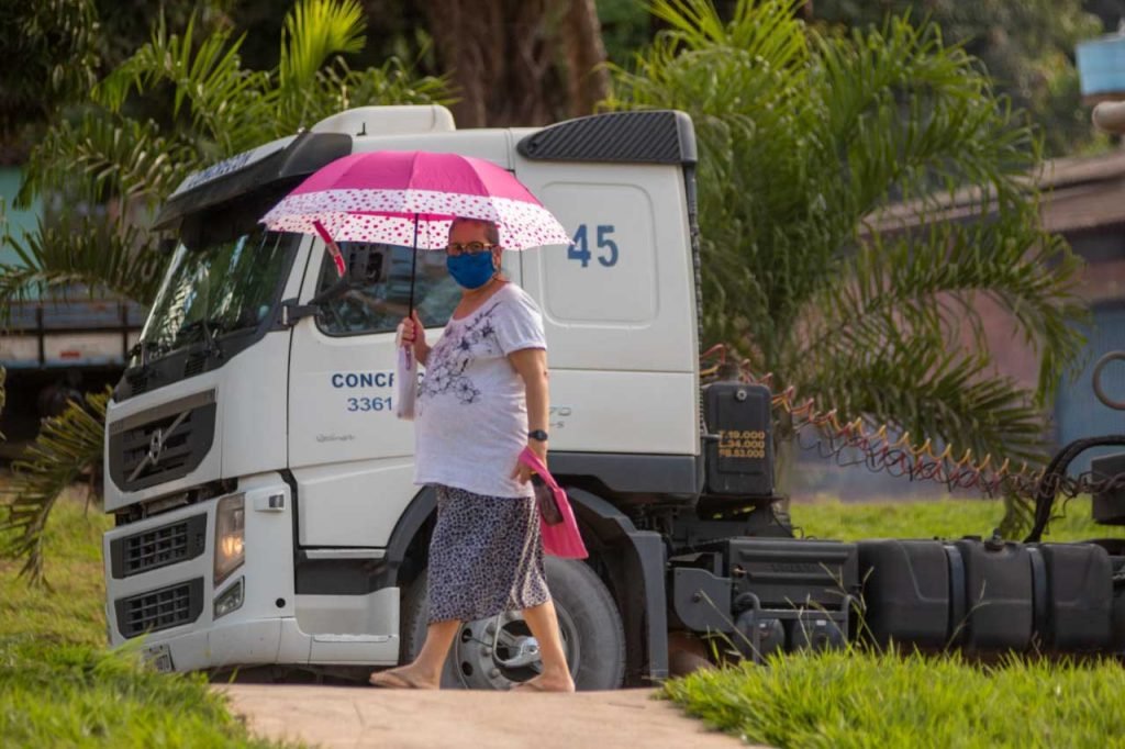 Mulher com máscara no rosto e sombrinha rosa na mão