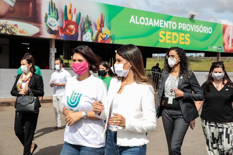 Duas mulheres andando de máscaras. Ao fundo, frase alojamento