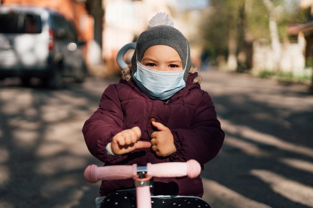 Criança usando casaco, máscara de proteção e andando de patinete
