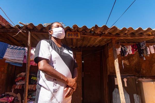 Mulher com máscara em frente de barraco