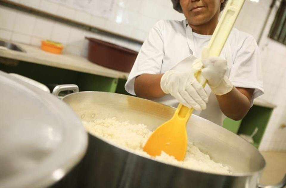 Merendeira com colher de pau mexendo em panelão