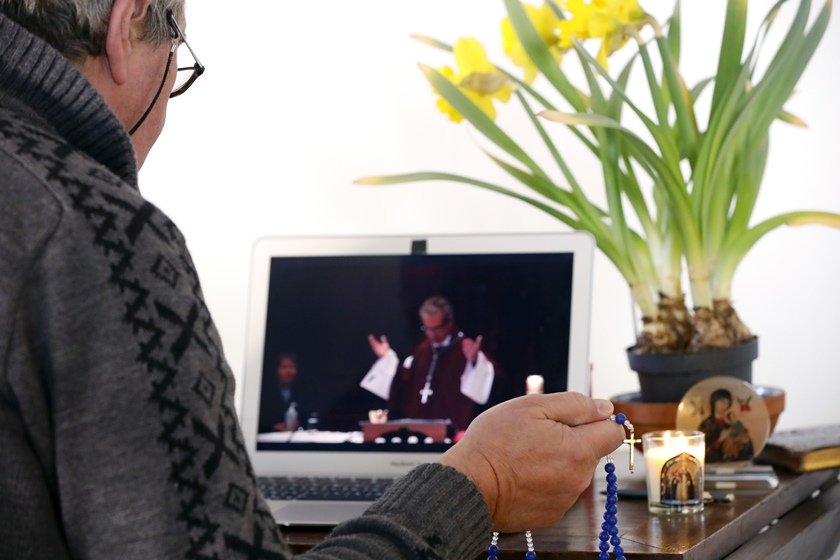 Homem acompanha missa on-line